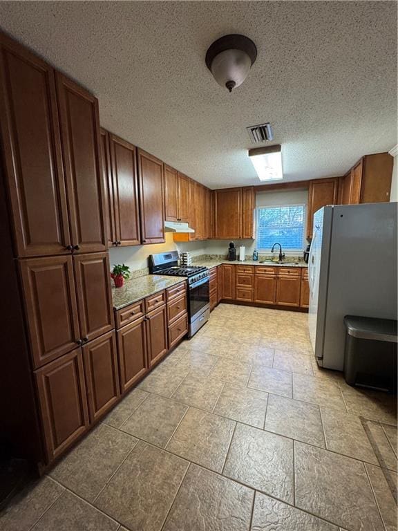 kitchen with sink, a textured ceiling, white fridge, and stainless steel range with gas stovetop