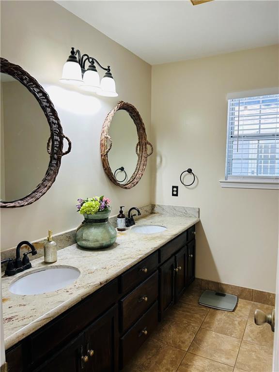 bathroom with baseboards, double vanity, a sink, and tile patterned floors