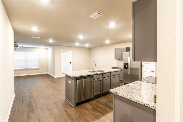 kitchen featuring gray cabinetry, stainless steel appliances, dark wood-type flooring, a sink, and an island with sink