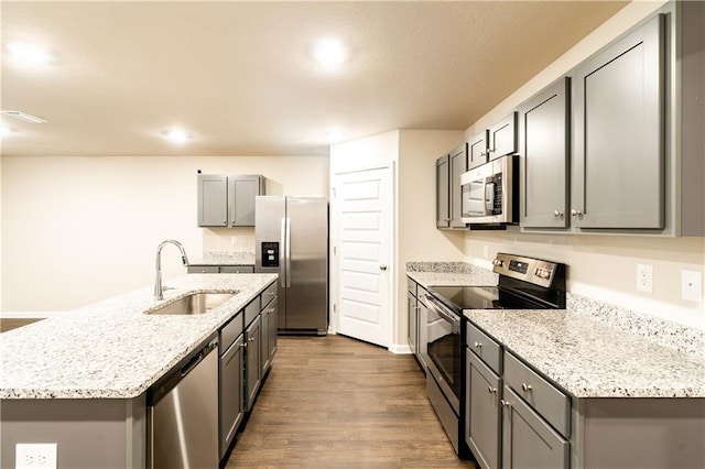 kitchen featuring light stone counters, gray cabinetry, dark wood-type flooring, a sink, and appliances with stainless steel finishes