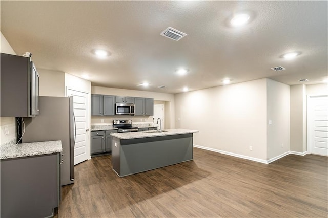 kitchen with dark wood finished floors, an island with sink, appliances with stainless steel finishes, gray cabinetry, and a sink