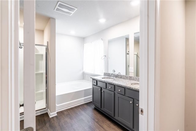 full bathroom featuring double vanity, visible vents, wood finished floors, a sink, and a bath