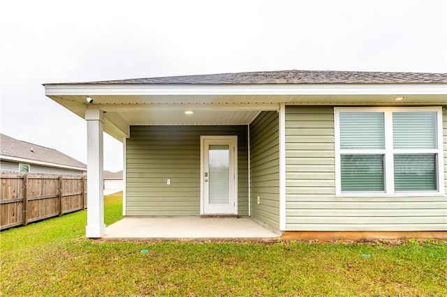 view of exterior entry featuring a yard, a patio area, and fence