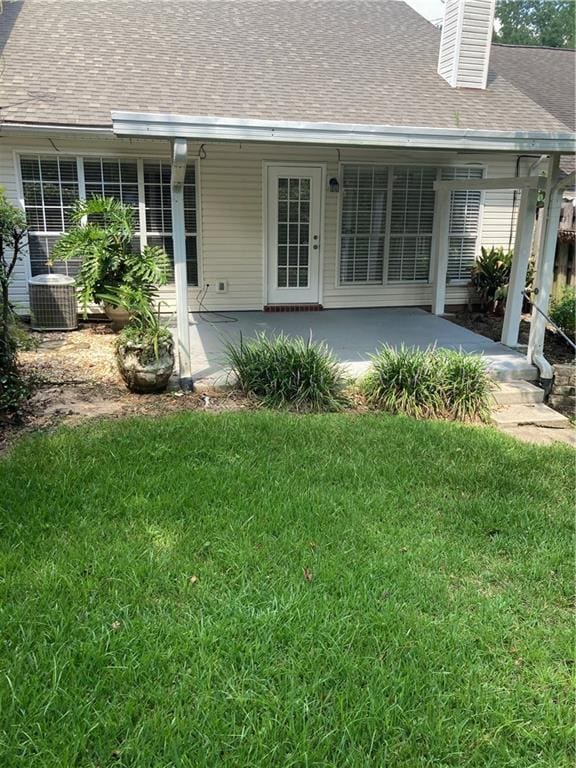 rear view of house featuring central air condition unit and a lawn