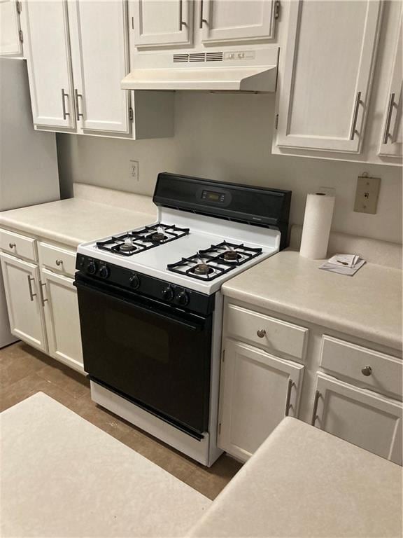 kitchen featuring white gas range oven, custom exhaust hood, tile patterned floors, white cabinetry, and stainless steel fridge