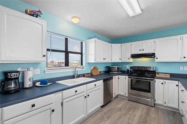 2528 Bridgeview Dr, Dauphin Island, AL 36528 - kitchen featuring appliances with stainless steel finishes, white cabinetry, dark countertops, light wood finished floors, and under cabinet range hood