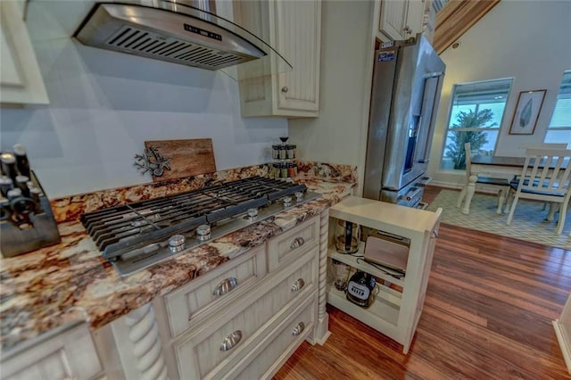 kitchen with light stone counters, ventilation hood, stainless steel appliances, and wood-type flooring