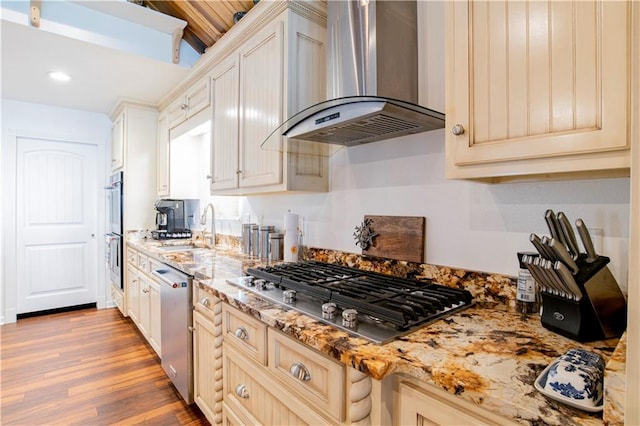 kitchen featuring appliances with stainless steel finishes, sink, light hardwood / wood-style floors, light stone countertops, and wall chimney exhaust hood