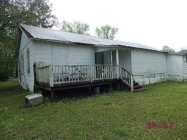 rear view of property with metal roof, a wooden deck, and a yard