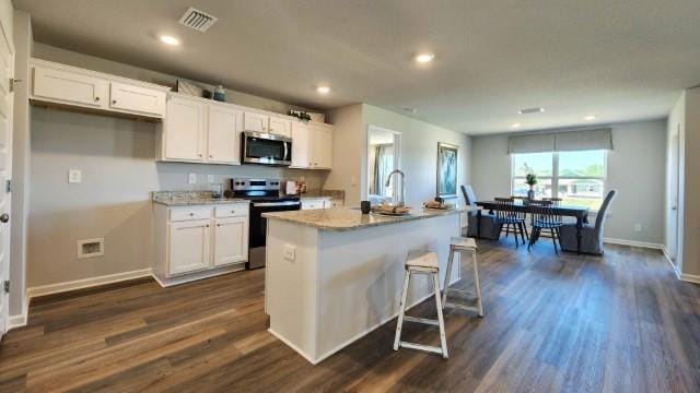 kitchen featuring stainless steel appliances, white cabinetry, dark wood-type flooring, and an island with sink