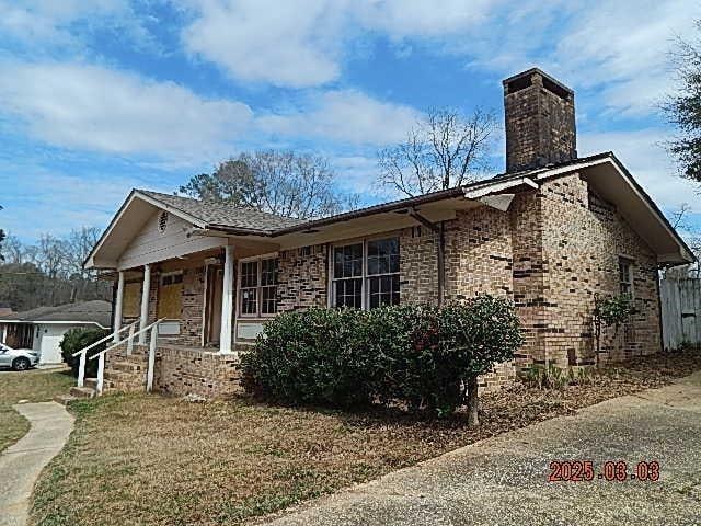 single story home with a chimney, a porch, and brick siding