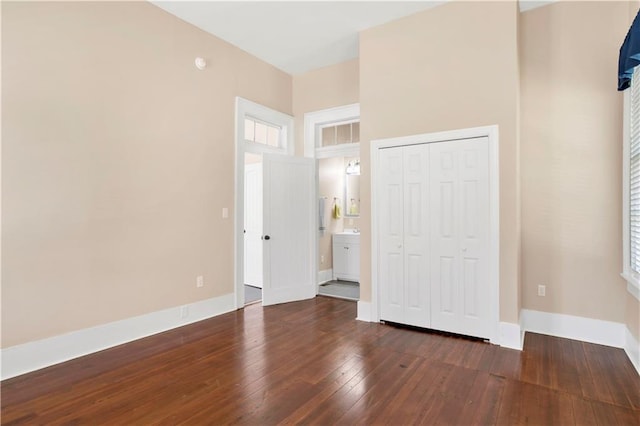 unfurnished bedroom featuring a closet, connected bathroom, multiple windows, and dark hardwood / wood-style floors