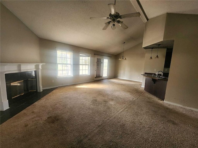 unfurnished living room featuring dark colored carpet, lofted ceiling, a fireplace with flush hearth, ceiling fan, and a textured ceiling