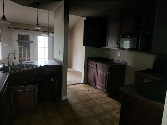 kitchen with dark brown cabinets, dark countertops, a sink, and decorative light fixtures