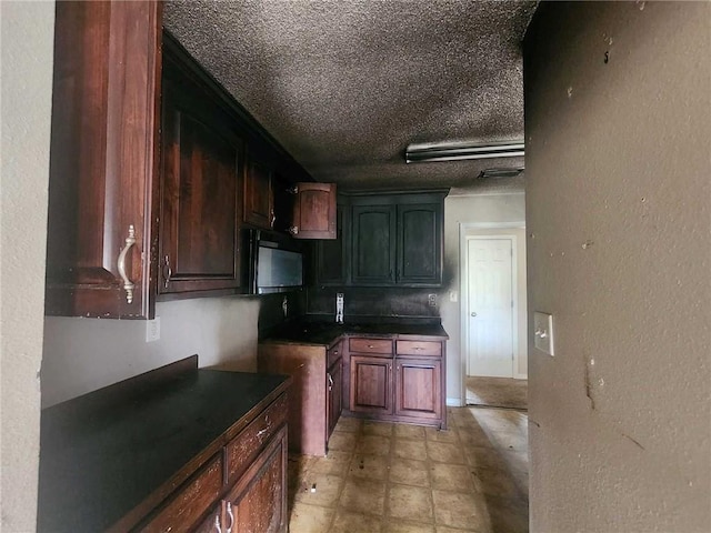 kitchen with a textured ceiling, a textured wall, dark countertops, and black microwave