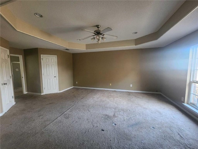 empty room with baseboards, a raised ceiling, a textured ceiling, and carpet flooring