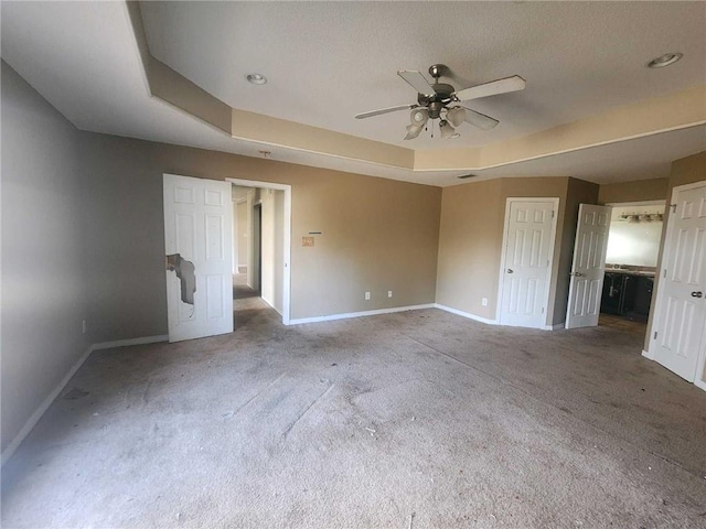 unfurnished bedroom featuring carpet, baseboards, a raised ceiling, and ensuite bathroom