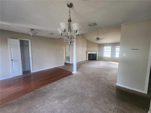 unfurnished living room with lofted ceiling, ceiling fan with notable chandelier, a fireplace, visible vents, and dark carpet