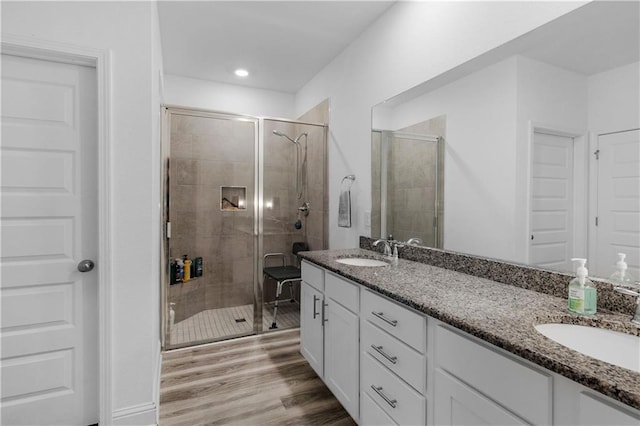 full bathroom featuring a shower stall, wood finished floors, double vanity, and a sink