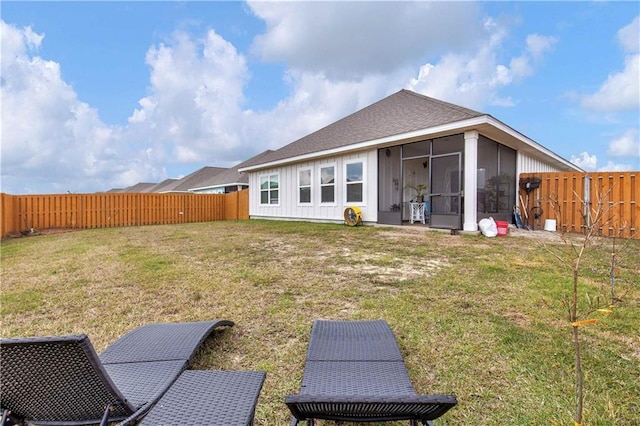 rear view of house with a yard, a fenced backyard, a sunroom, and roof with shingles