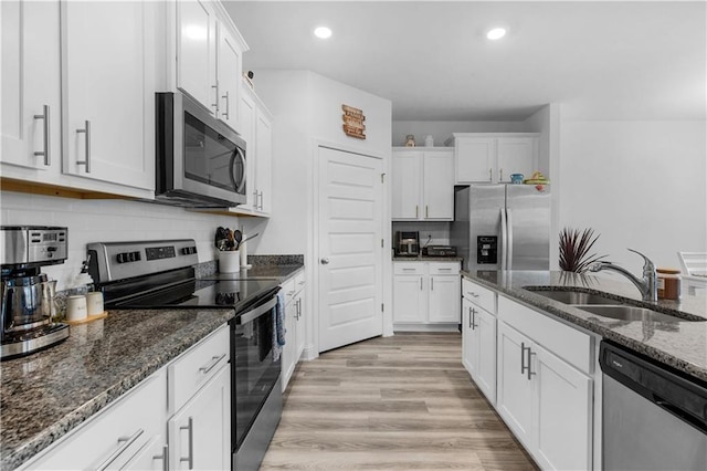 kitchen featuring tasteful backsplash, appliances with stainless steel finishes, light wood-style floors, white cabinets, and a sink