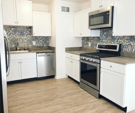 kitchen with white cabinets, backsplash, and appliances with stainless steel finishes