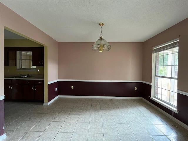 unfurnished dining area featuring a textured ceiling, sink, and a chandelier