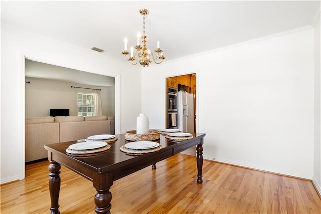 dining area with a notable chandelier, light wood finished floors, visible vents, and crown molding