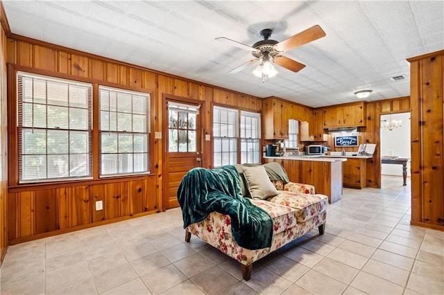 living room with ceiling fan, wood walls, and a healthy amount of sunlight