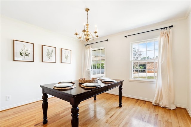 dining space featuring light wood finished floors, crown molding, baseboards, and a notable chandelier