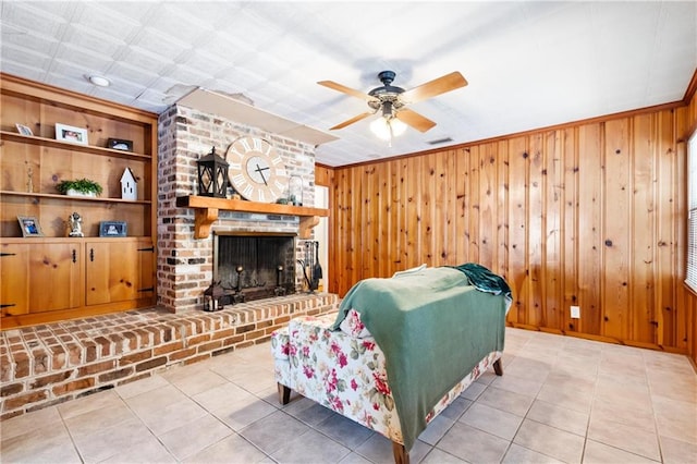 tiled living room with a fireplace, wooden walls, ceiling fan, and brick wall