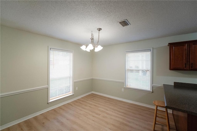 unfurnished dining area featuring a textured ceiling, a notable chandelier, and light wood-type flooring