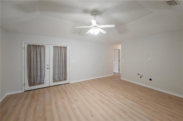 spare room featuring a raised ceiling, ceiling fan, light wood-type flooring, and french doors