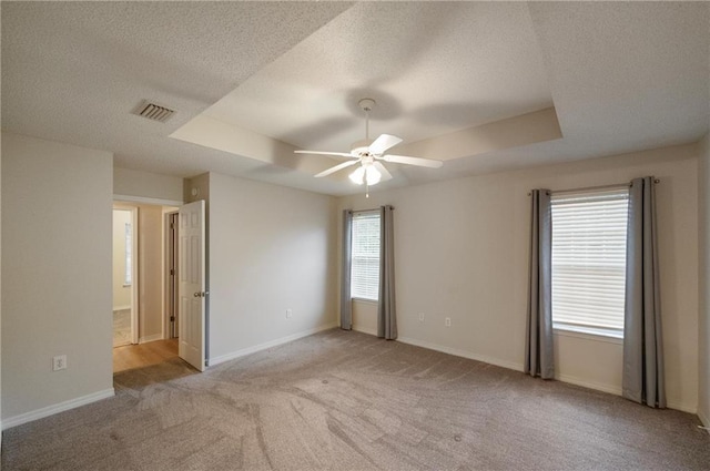 empty room with light carpet, a wealth of natural light, a raised ceiling, and ceiling fan