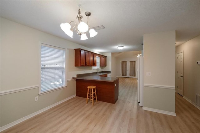 kitchen with sink, light hardwood / wood-style flooring, white refrigerator, kitchen peninsula, and pendant lighting