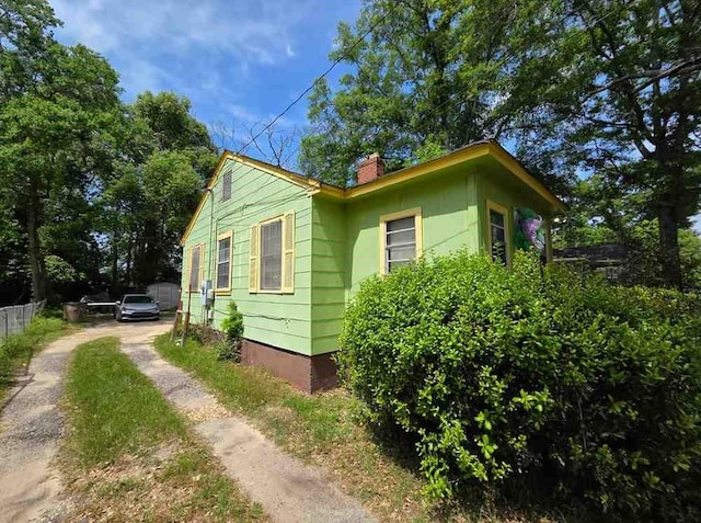 view of home's exterior featuring a chimney, fence, and dirt driveway