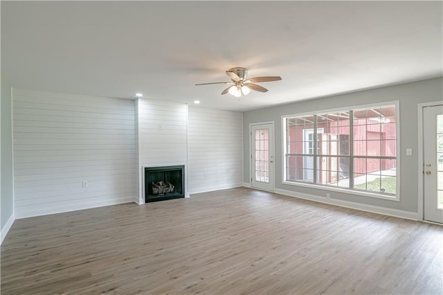 unfurnished living room featuring ceiling fan, a large fireplace, and wood-type flooring