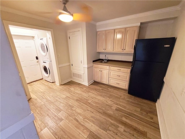 kitchen featuring light wood-type flooring, black fridge, ornamental molding, sink, and stacked washer / drying machine