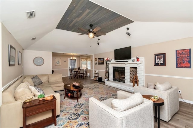 living room featuring vaulted ceiling, ceiling fan with notable chandelier, hardwood / wood-style floors, and a brick fireplace