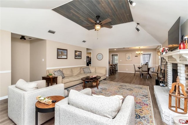 living room featuring vaulted ceiling, a brick fireplace, dark hardwood / wood-style floors, and ceiling fan with notable chandelier