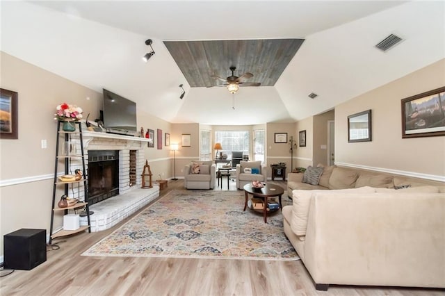 living room with vaulted ceiling, ceiling fan, a fireplace, and light hardwood / wood-style flooring