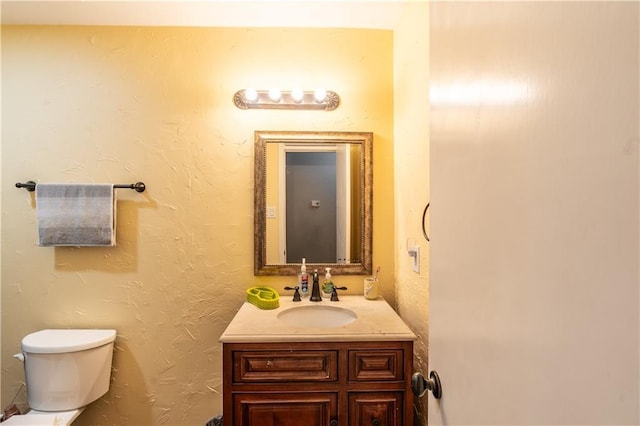 half bathroom with a textured wall, vanity, and toilet