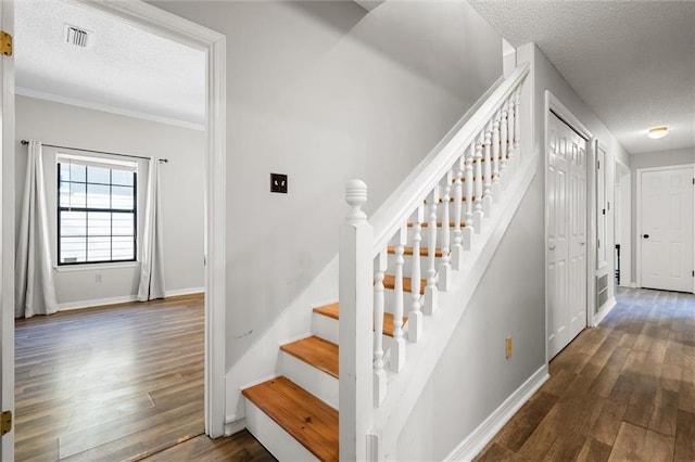 staircase featuring hardwood / wood-style flooring, ornamental molding, and a textured ceiling