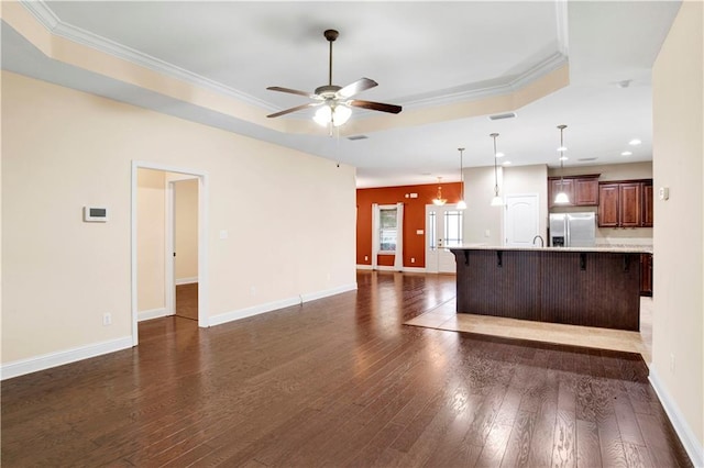 unfurnished living room featuring a tray ceiling, ceiling fan, dark hardwood / wood-style floors, and ornamental molding