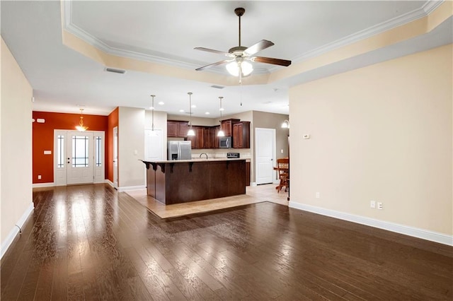 kitchen featuring a center island with sink, a raised ceiling, hanging light fixtures, dark hardwood / wood-style floors, and appliances with stainless steel finishes