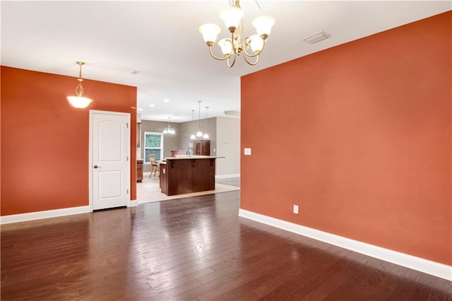 empty room with dark wood-type flooring and a notable chandelier