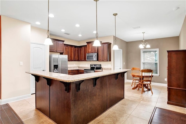 kitchen with a kitchen bar, appliances with stainless steel finishes, light stone counters, pendant lighting, and a chandelier