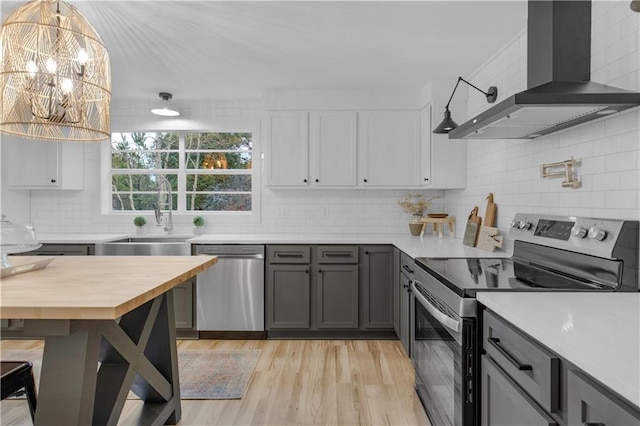 kitchen with wall chimney range hood, sink, gray cabinets, stainless steel appliances, and decorative light fixtures