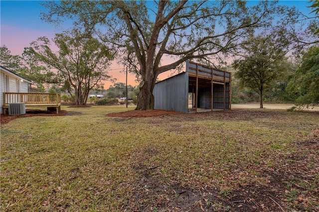 yard at dusk with cooling unit, an outdoor structure, and a deck