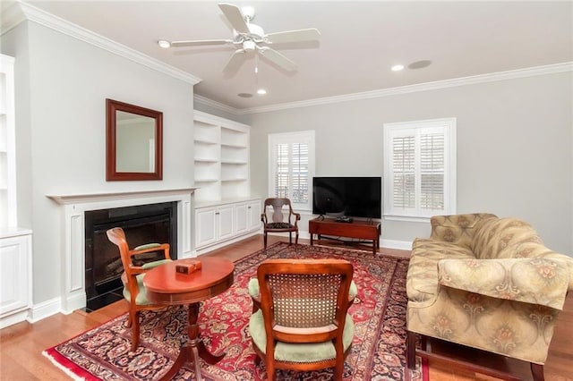 living room with built in features, light wood-style flooring, ornamental molding, a fireplace with flush hearth, and baseboards